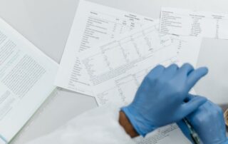Gloved hands reviewing printed blood test lab results, representing annual blood work in preventive medicine.