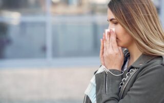 Woman sneezing outdoors into a tissue, experiencing spring allergy symptoms in nature.